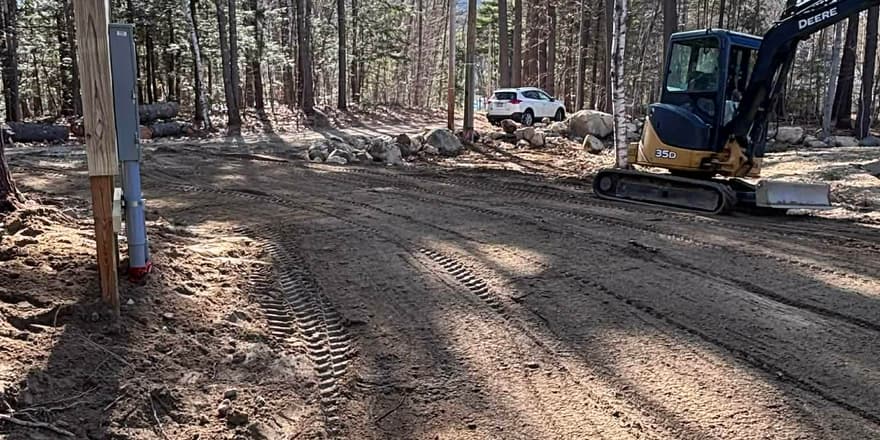 Excavator grading a wooded driveway